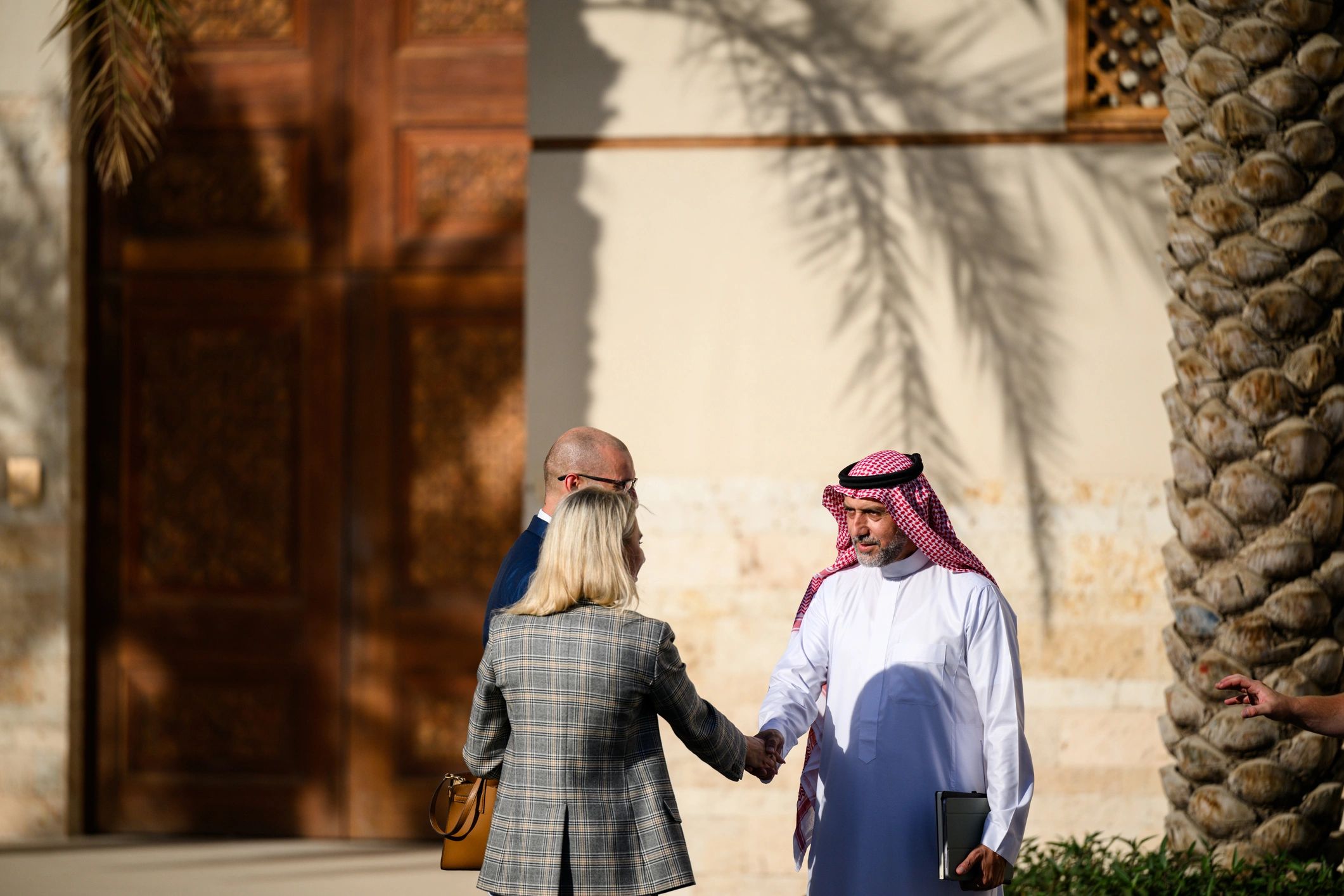 Wide shot of a professional woman greeting a Saudi business man in a partnership meeting outdoors near an office building